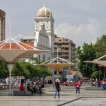 A vibrant city square featuring unique canopies and historic architecture, bustling with people.