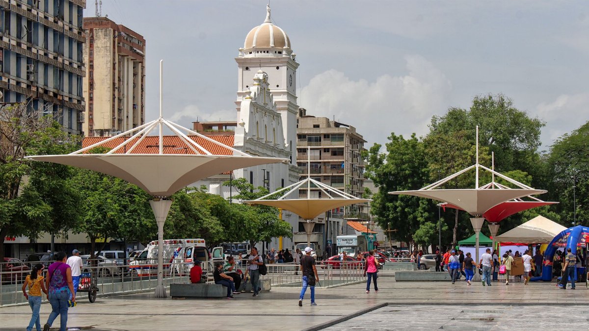 A vibrant city square featuring unique canopies and historic architecture, bustling with people.