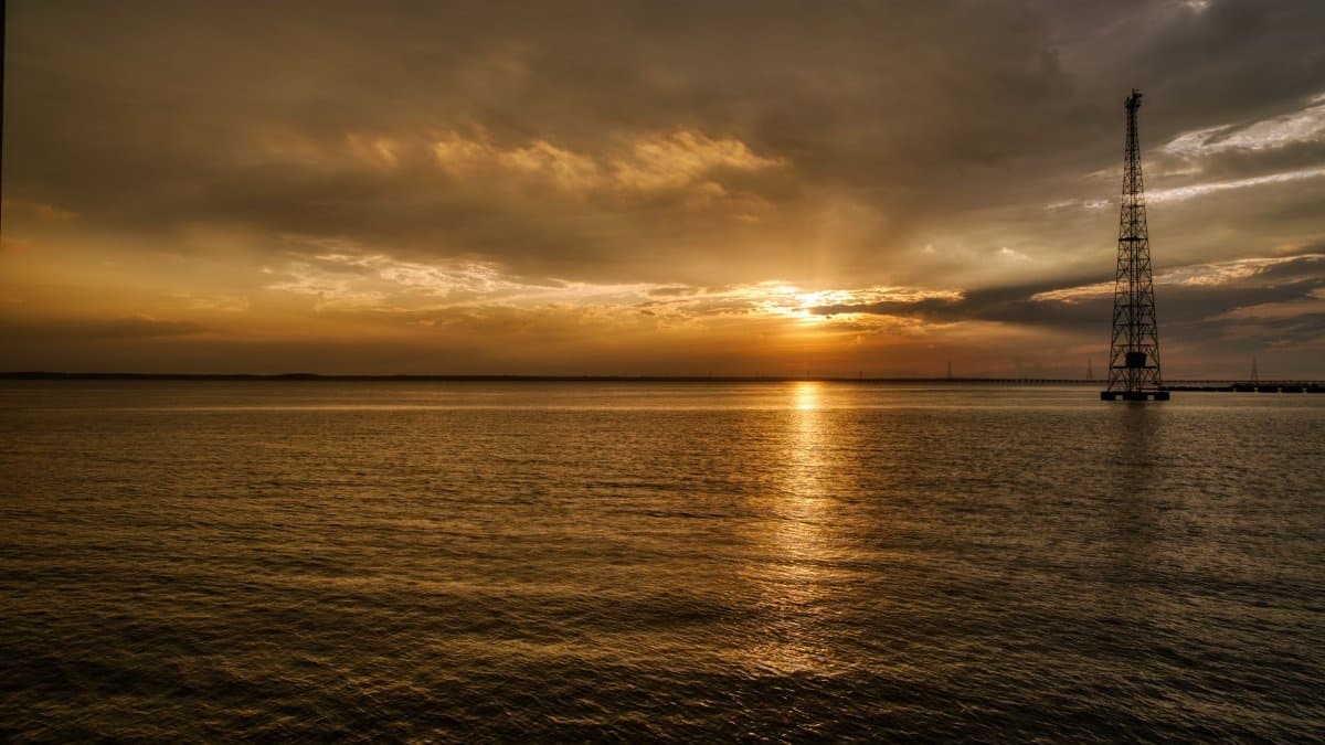 Dramatic golden hour sunset over calm ocean in Newport News, showcasing reflected tower silhouette.