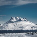 Breathtaking view of snowy mountains in Nuuk, Greenland surrounded by icy waters and clear blue skies.