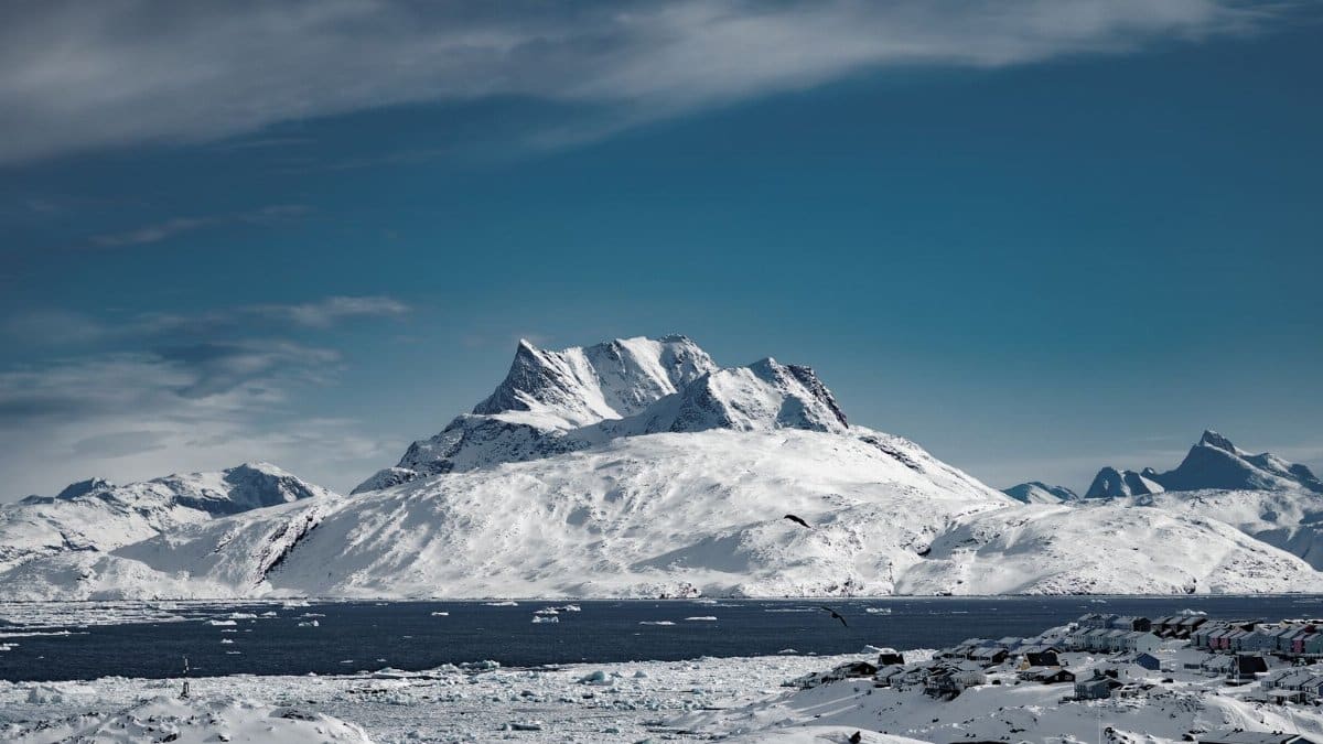 Breathtaking view of snowy mountains in Nuuk, Greenland surrounded by icy waters and clear blue skies.