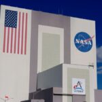 The iconic NASA Vehicle Assembly Building at Kennedy Space Center in bright daylight.