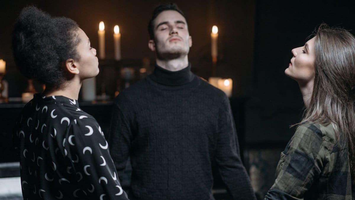 Three individuals engage in a spiritual meditation surrounded by candlelight.