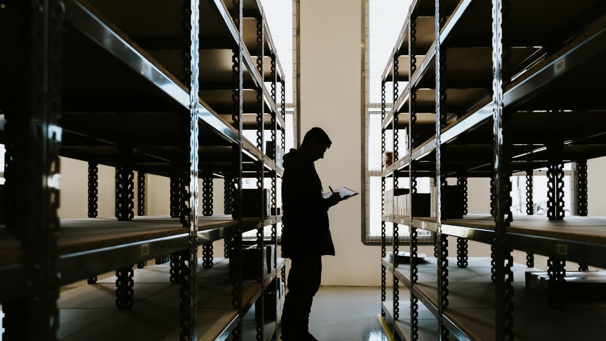 Silhouette of a person checking inventory in an empty warehouse with racks.