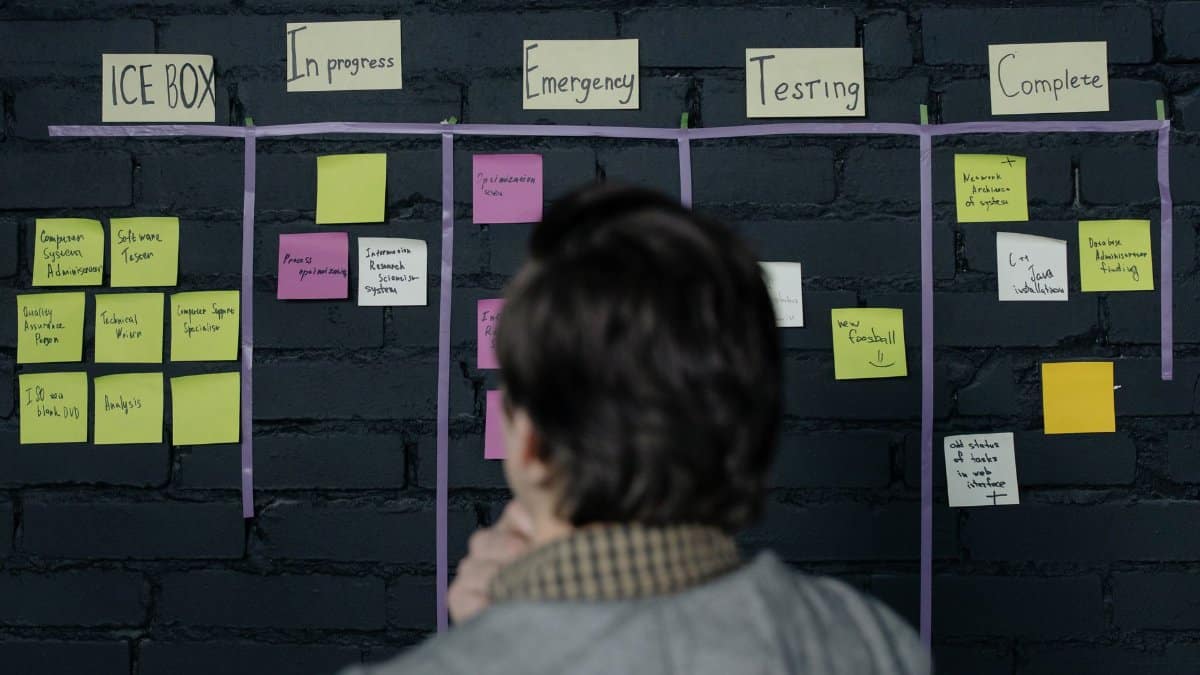A man in an office reviews a scrum task board filled with sticky notes, planning strategy and organization.
