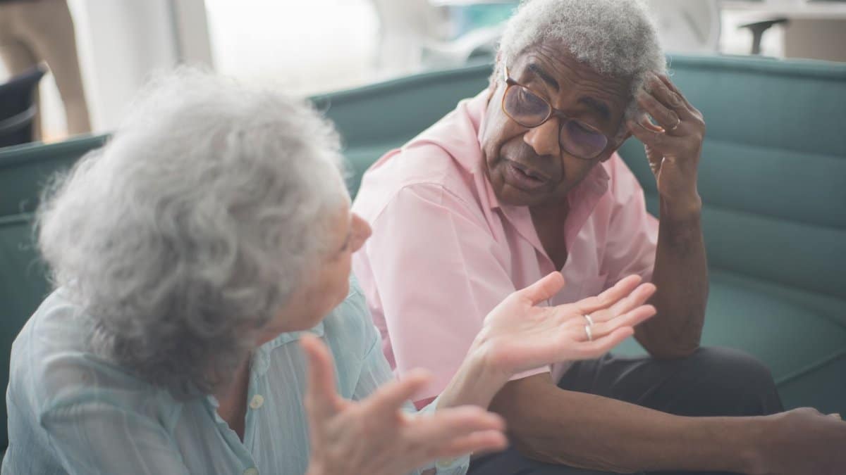 Two senior adults having a thoughtful discussion on a comfortable couch indoors.