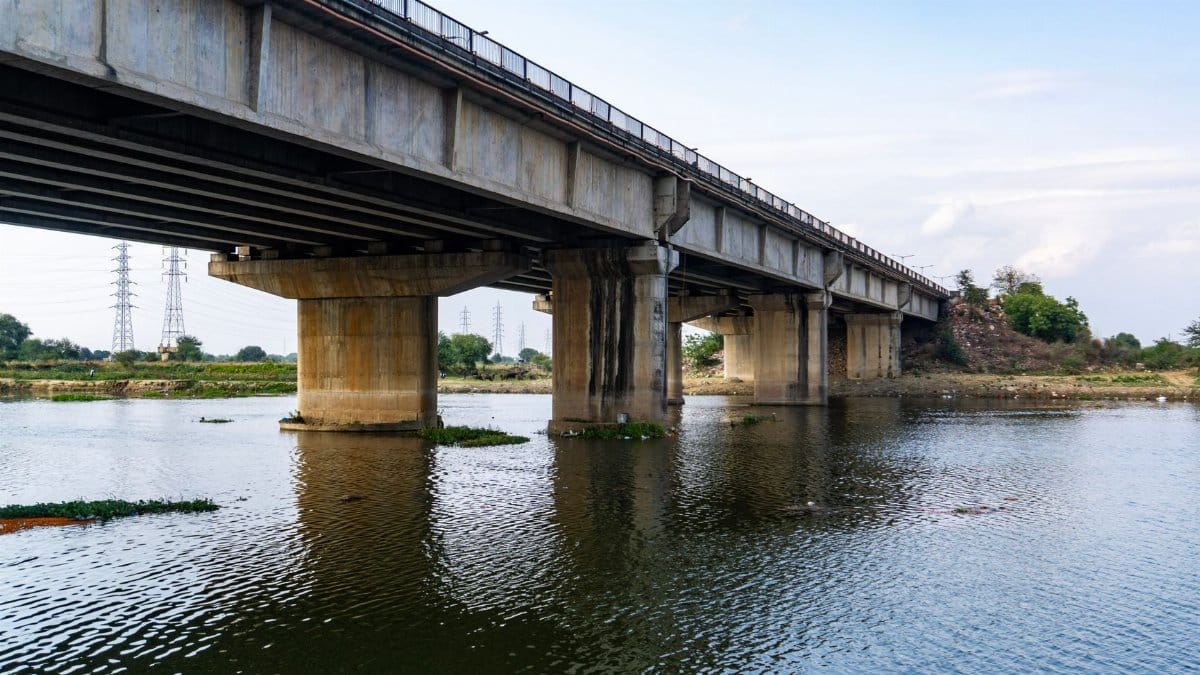 A large concrete bridge spanning a calm river under a clear sky, showcasing modern infrastructure.