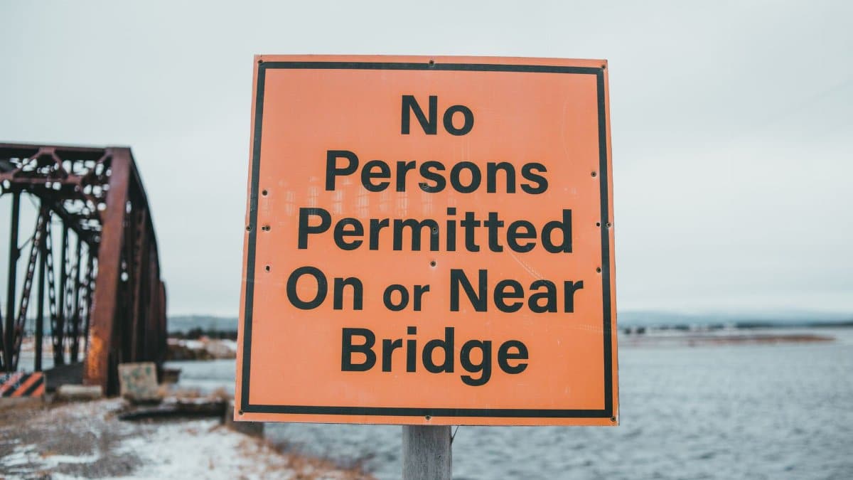 Restrictive signboard with inscription on snowy coast against aged bridge and rippled ocean in daytime