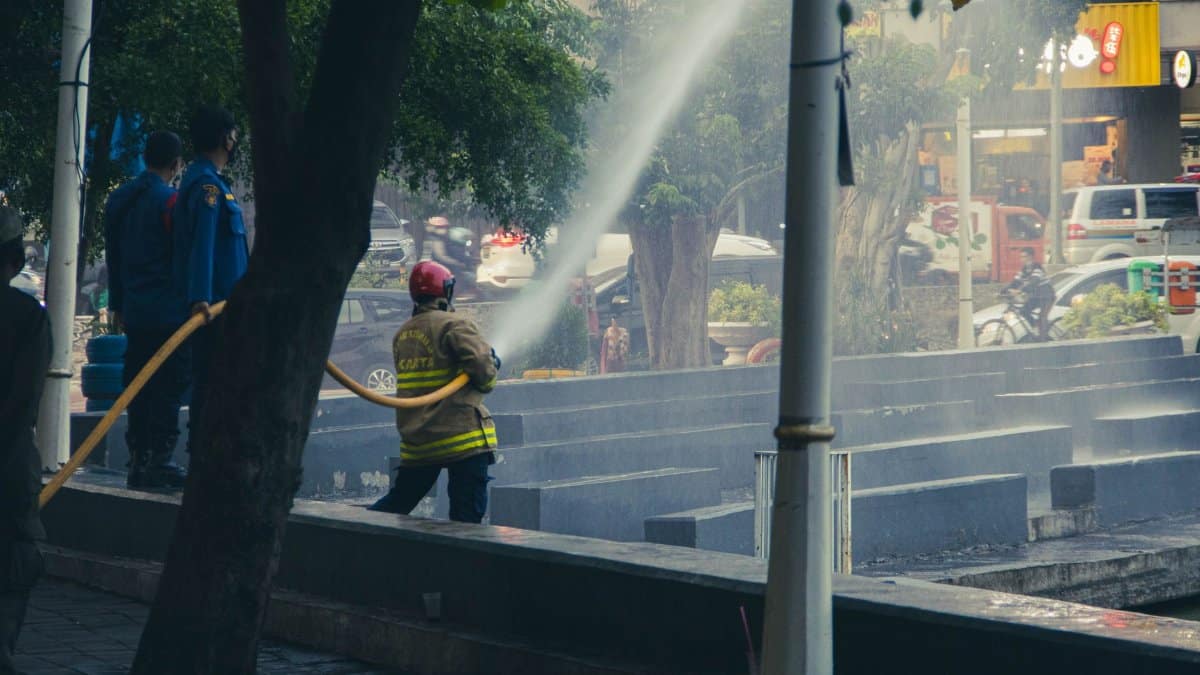Firefighters using a hose to combat a fire with police observing in an urban setting.