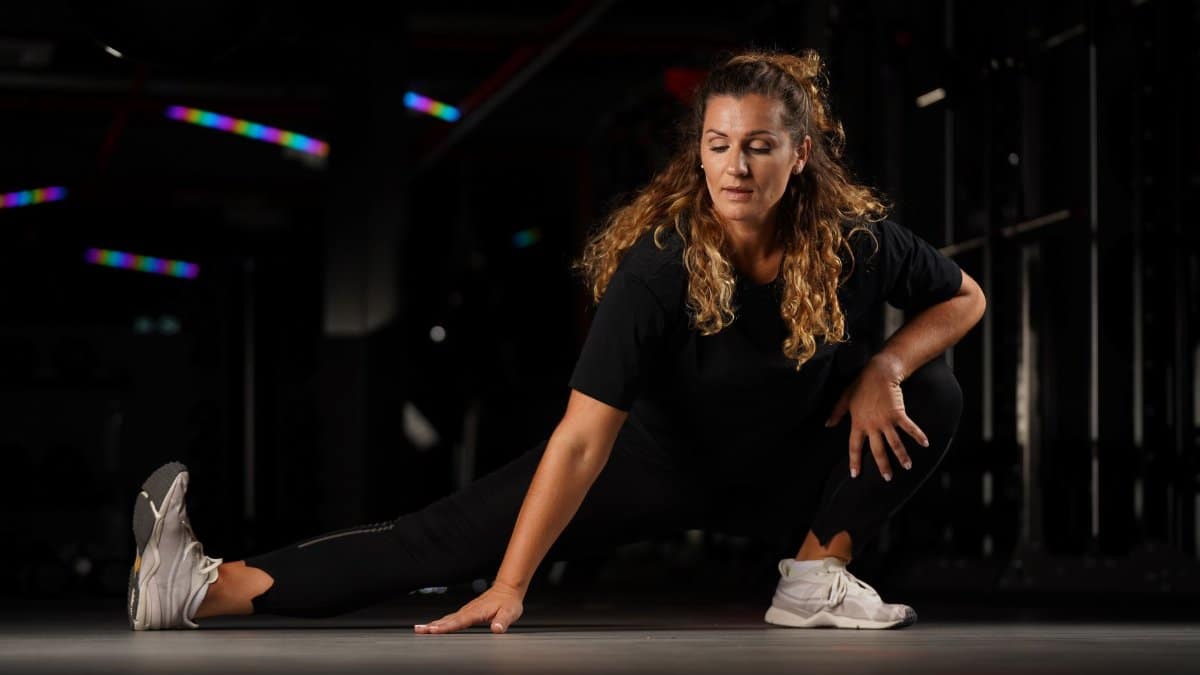 Woman stretching in a dimly lit gym in Riga, Latvia, focused on flexibility.