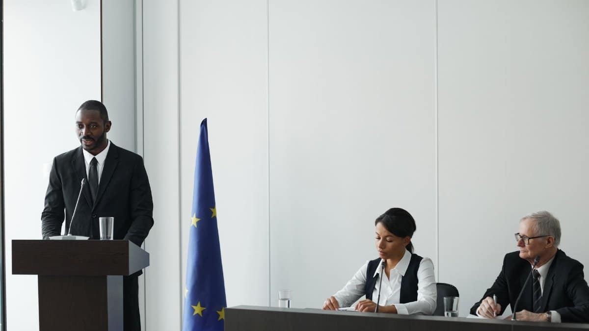 Professional business conference with EU flag, diverse speakers in suits discussing diplomacy.