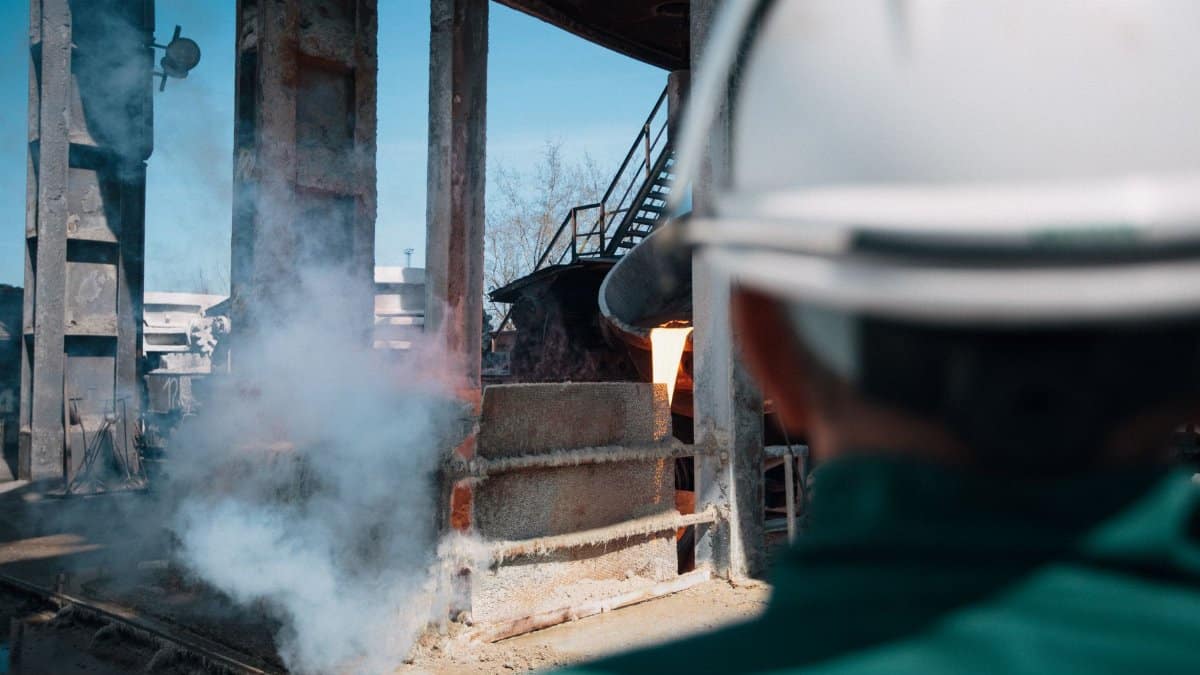 A worker in a hard hat observes a smelting process at an industrial plant.