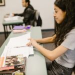 Young woman focused on exam preparations in a college classroom, writing notes on test papers.