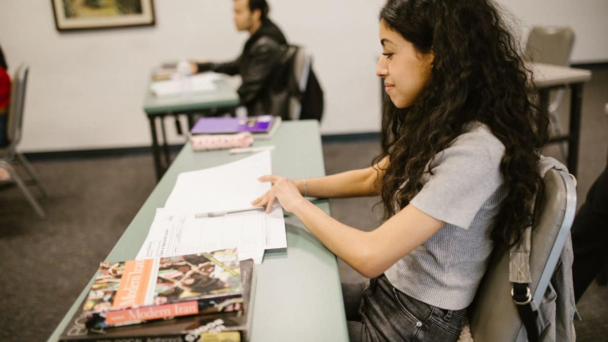 Young woman focused on exam preparations in a college classroom, writing notes on test papers.