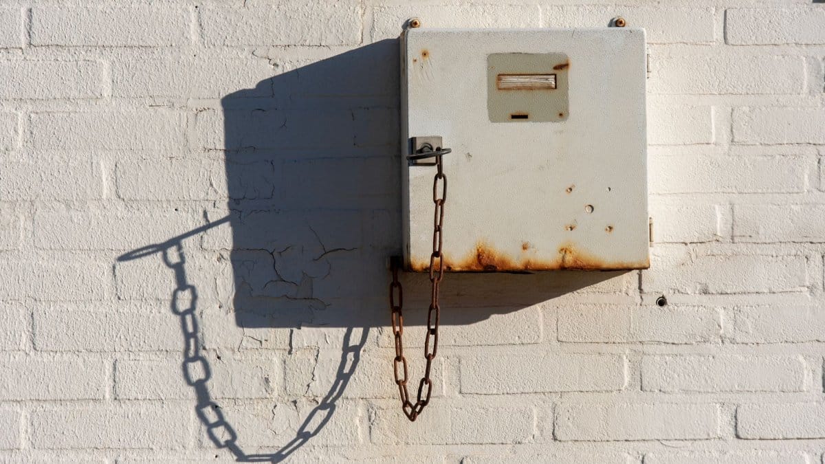 Rusty metallic utility box with chain on a white brick wall capturing shadows and texture.