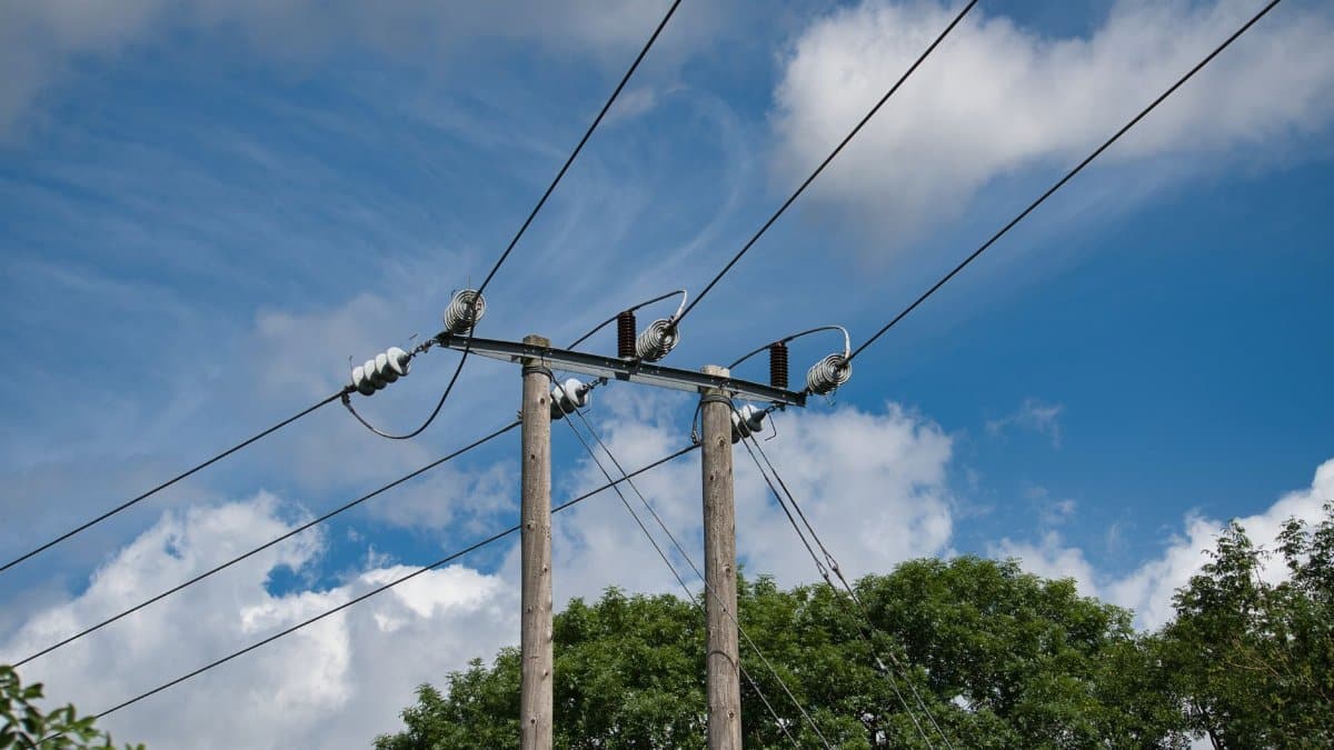 Power lines and wooden utility poles under a bright blue sky with scattered clouds.