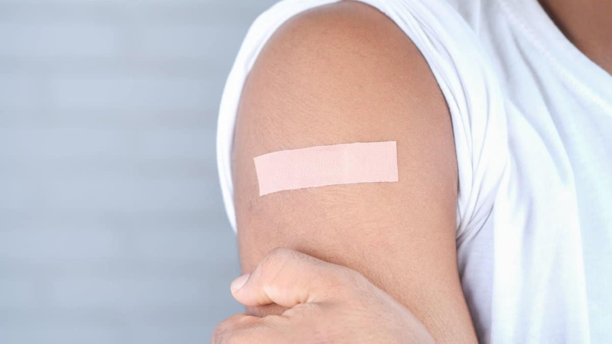 A close-up image of an adult with a bandage on the upper arm, likely after vaccination.