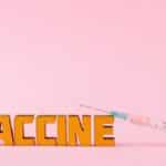 Close-up of a syringe and vaccine vial on a pink backdrop for health concepts.