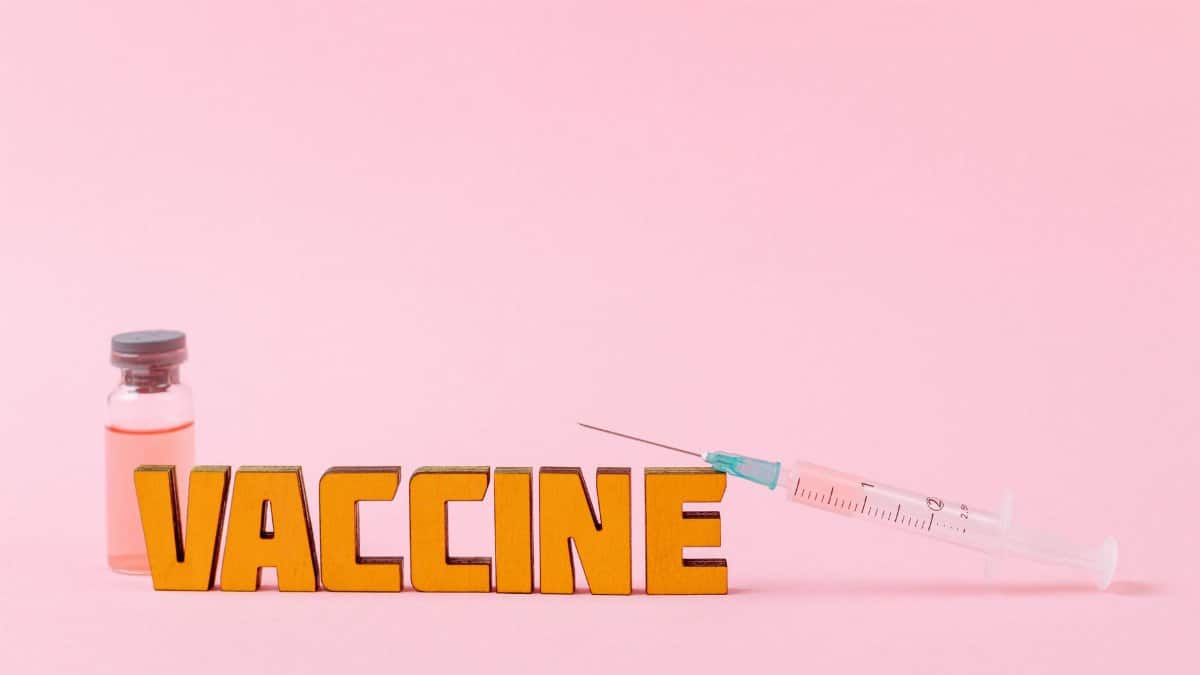 Close-up of a syringe and vaccine vial on a pink backdrop for health concepts.