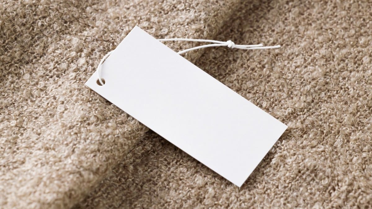Close-up of a blank white price tag on textured beige fabric, ideal for branding use.