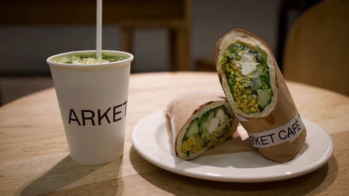 Delicious vegetarian wrap with green juice served at Arket Café on a wooden table.