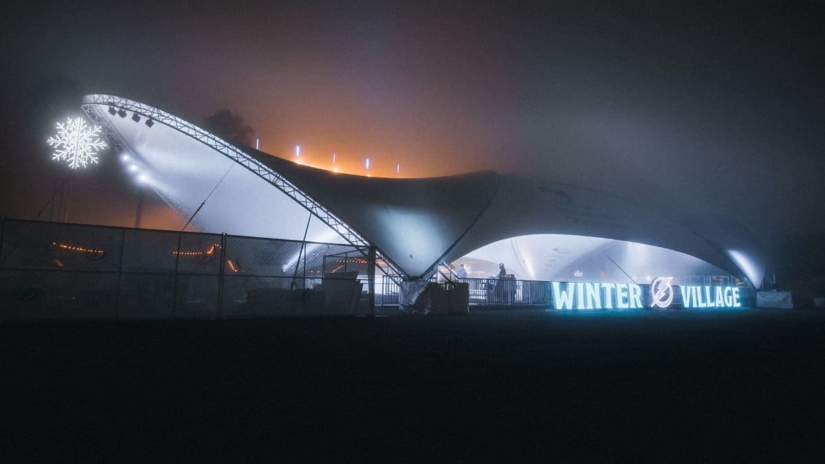 A glowing winter village tent with lights and snowflake decor at night, showcasing a festive ambiance.