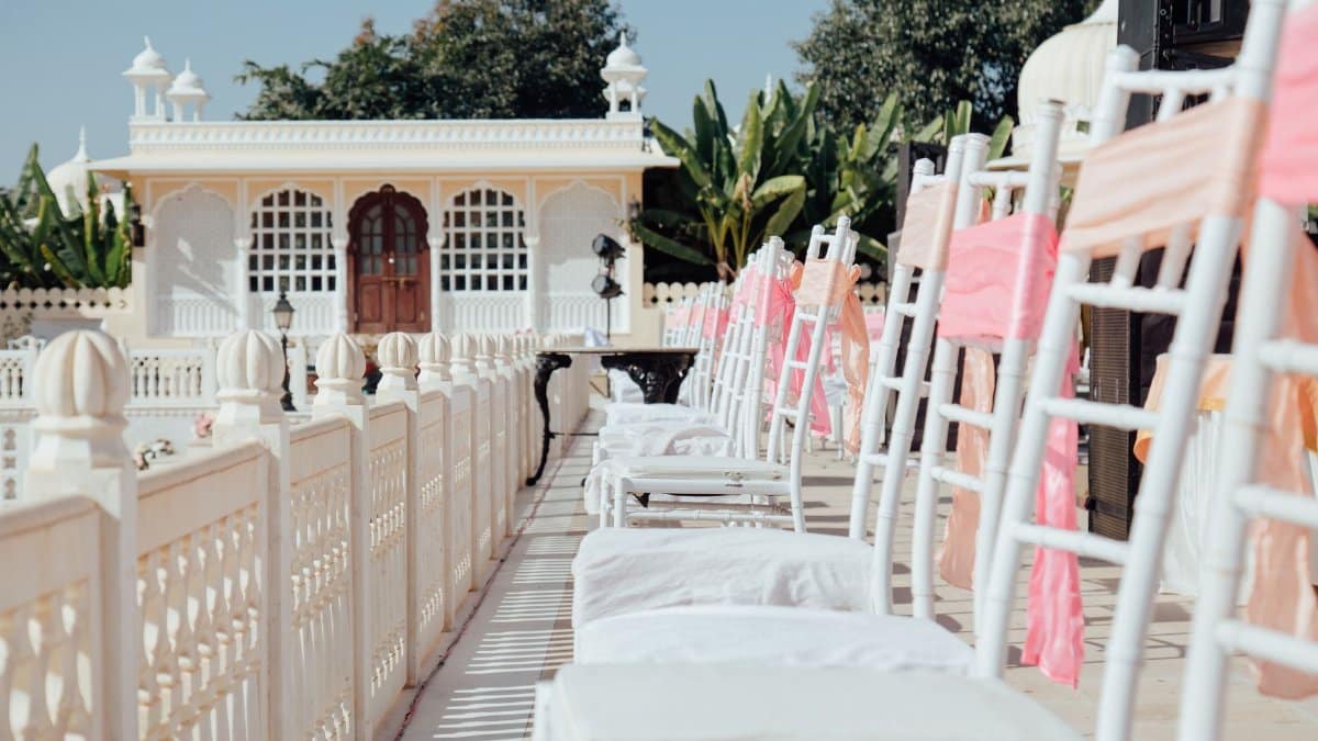 Beautifully decorated outdoor wedding venue with white chairs and pastel drapes in an Indian courtyard.