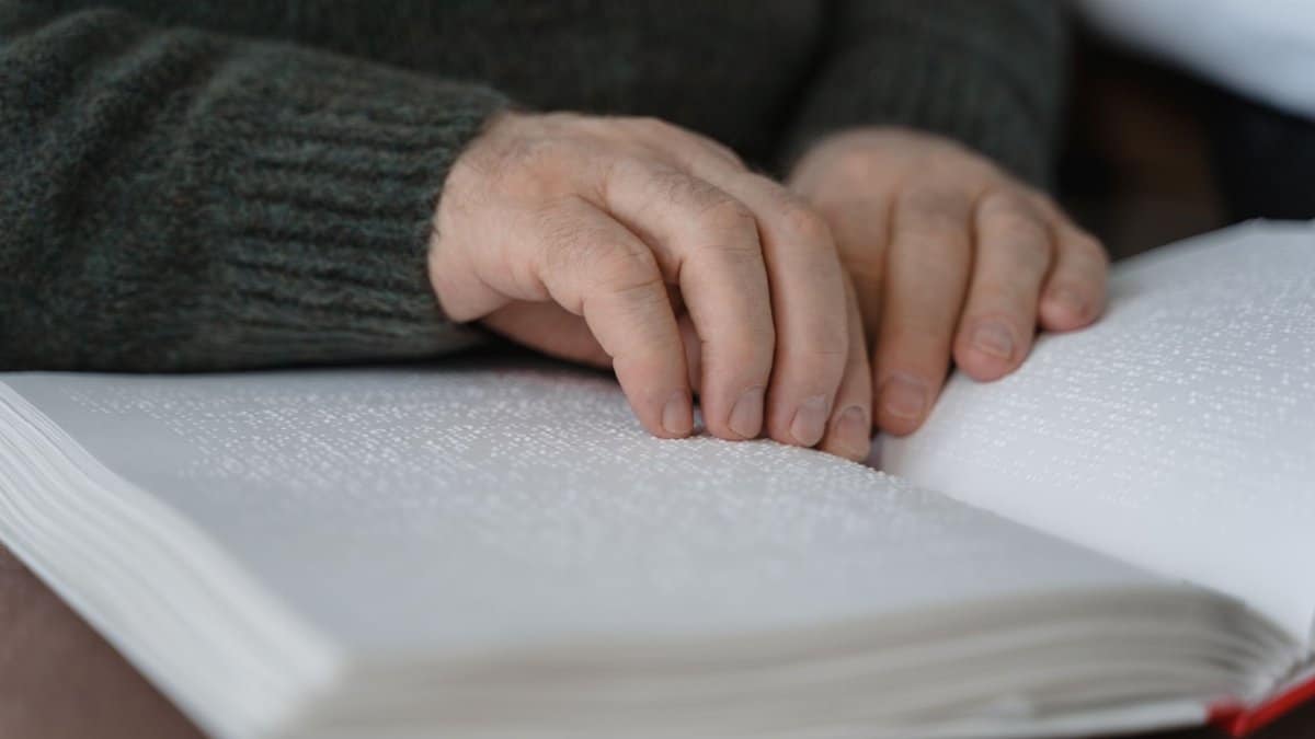 Close-up of hands reading a braille book, emphasizing accessibility and tactile learning.