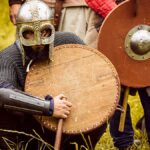 Medieval warriors in armor at a reenactment event, showcasing shields and helmets.