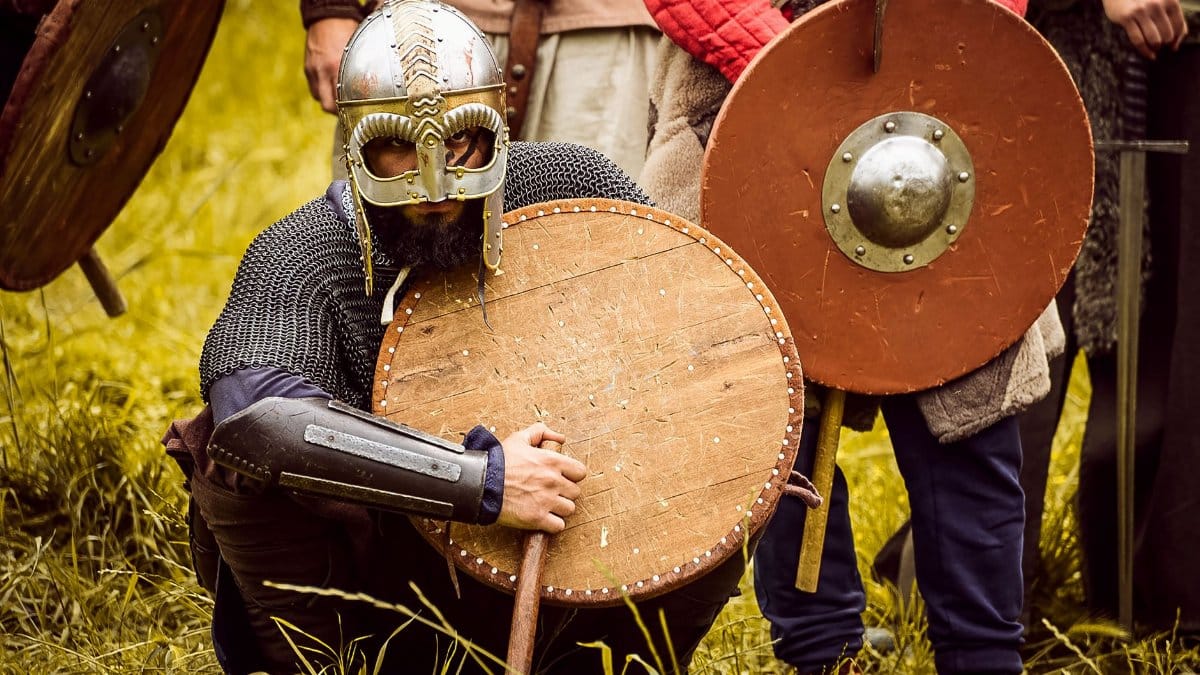 Medieval warriors in armor at a reenactment event, showcasing shields and helmets.