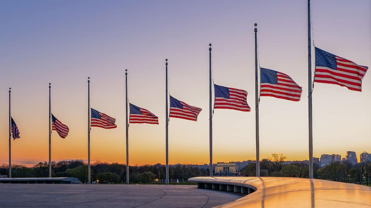 American flags at half-mast surround the Washington Monument during a vibrant sunset.