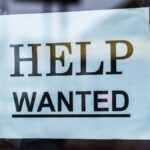 Close-up of a Help Wanted sign taped to a glass window in a storefront.