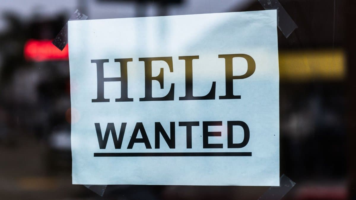 Close-up of a Help Wanted sign taped to a glass window in a storefront.