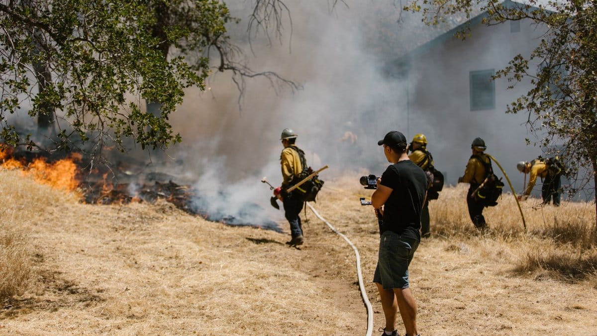 Firefighters in protective gear combating a spreading wildfire near a home.