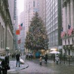 A snowy winter scene in New York City with a decorated Christmas tree and bustling street life.