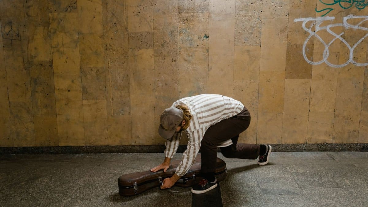 Man setting up guitar case as a street musician indoors against a graffiti wall.