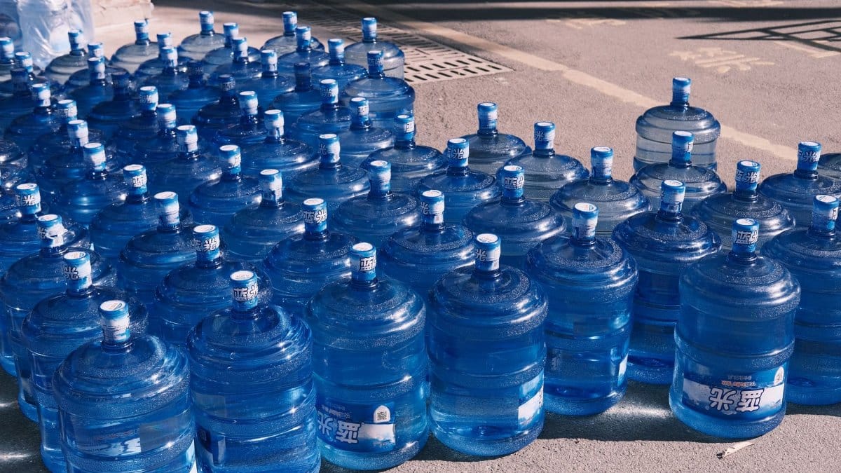 A collection of blue plastic water jugs lined up on an urban street in sunlight.