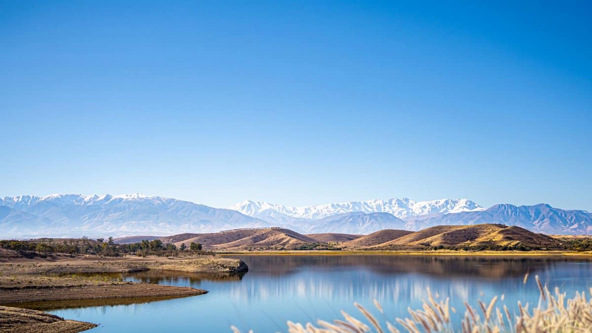 Tranquil mountain lake under clear blue sky with snow-capped peaks reflecting on the water.