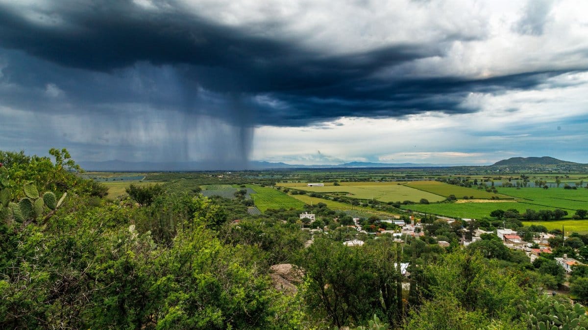 Dark storm clouds and heavy rain over lush green fields, creating a dramatic landscape scene.