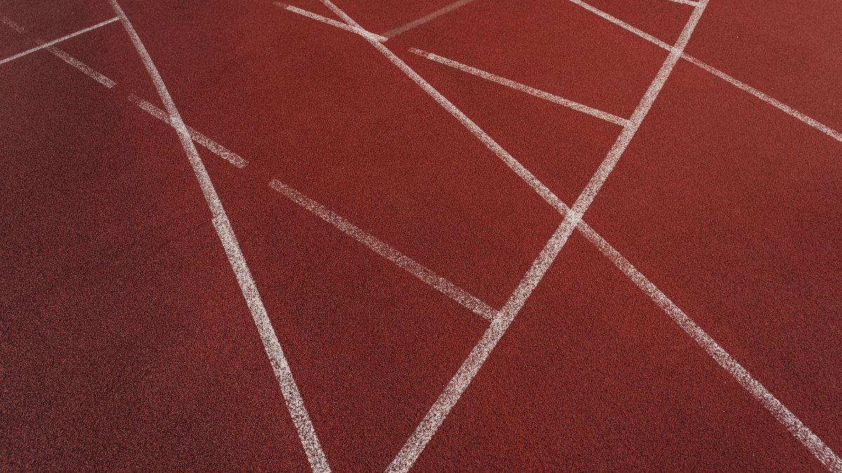 A detailed view of a red sports track showing intersecting white lines creating geometric patterns.