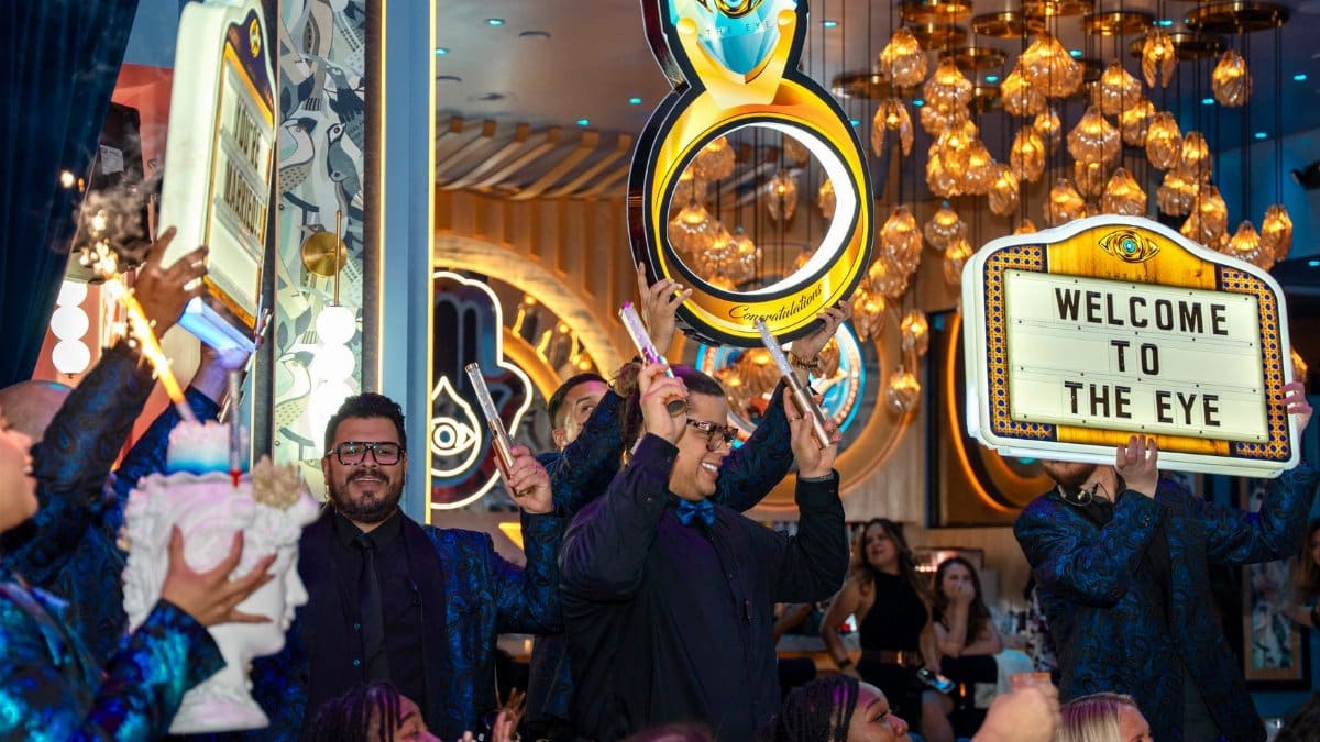 Guests celebrate in a vibrant, upscale venue with 'Welcome To The Eye' signs and festive atmosphere.