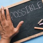 A hand on a chalkboard with 'Possible' written in chalk signifies optimism and potential.