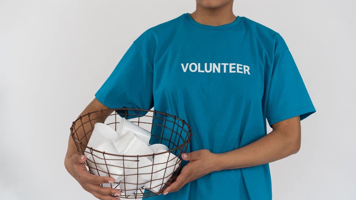 Person in blue shirt holding a metal basket filled with disposable cups, promoting environmental awareness.