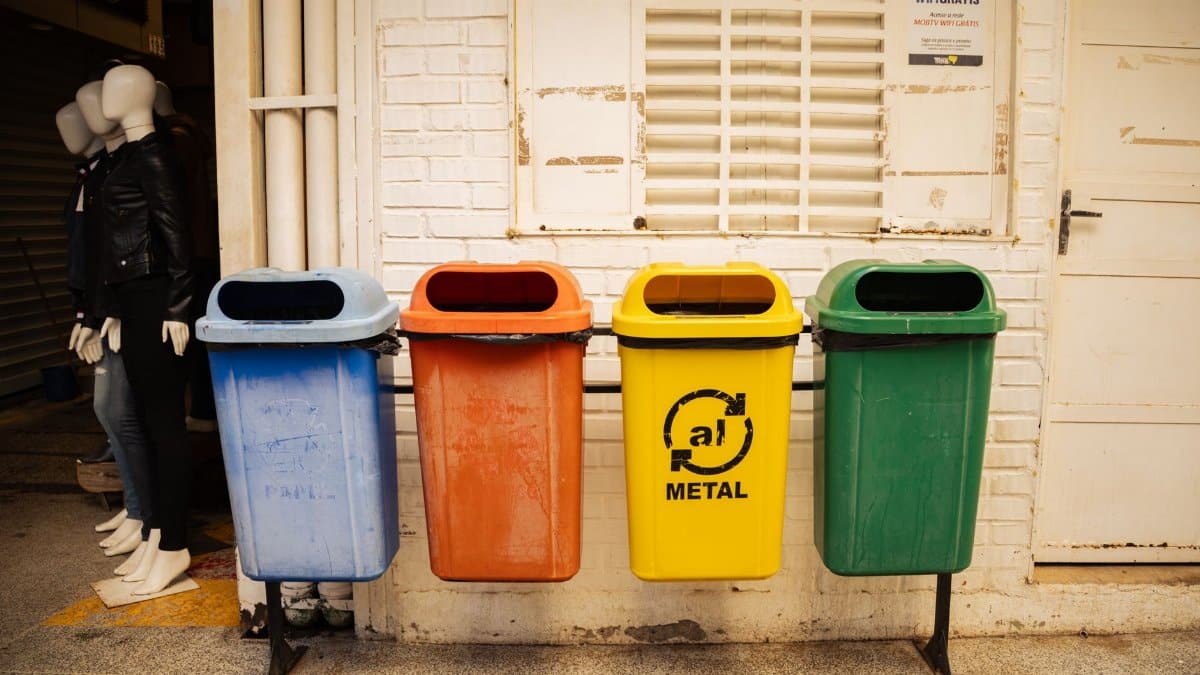 Four colorful recycling bins for different materials against a brick wall in an urban environment.