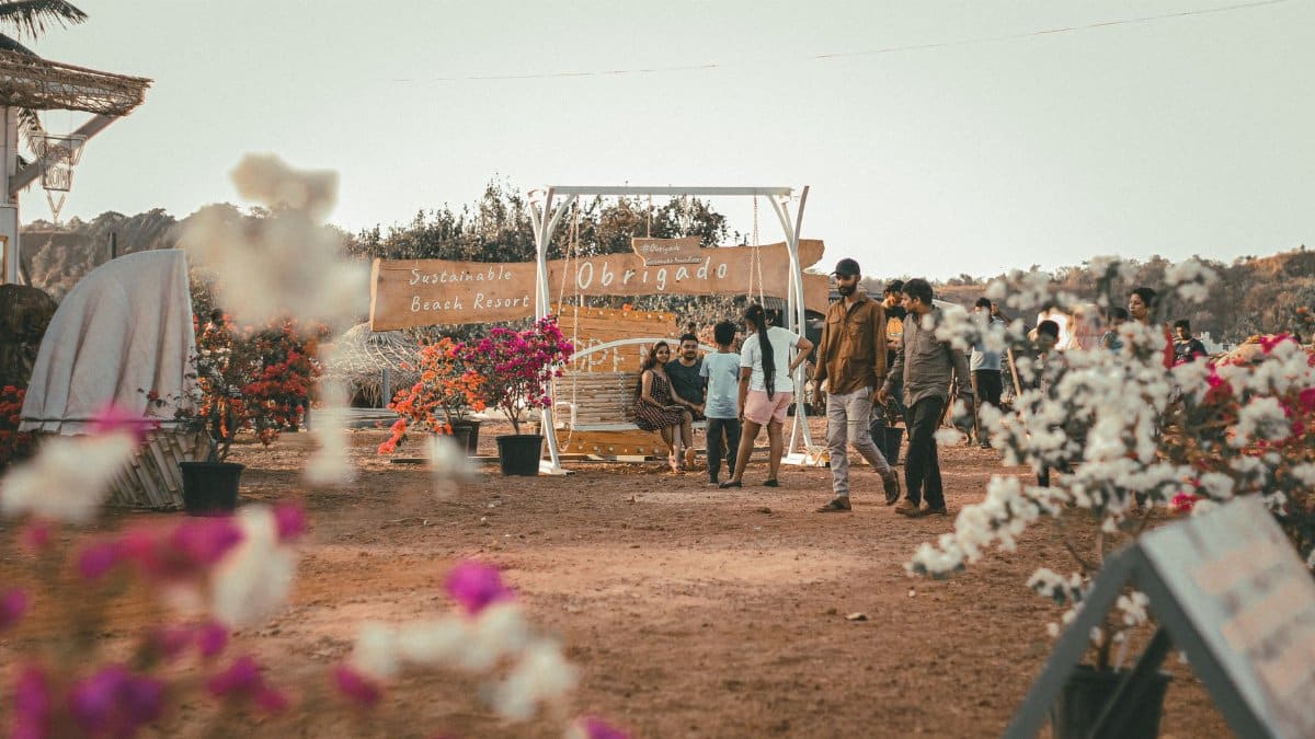 A festival scene at a beach resort with people, colorful flowers and a sign reading 'Obrigado'.