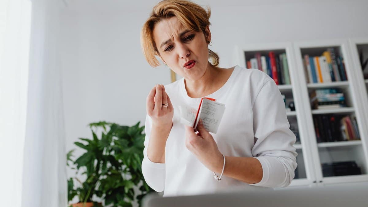 A concerned woman reviews her finances while holding receipts, showing a worried expression.
