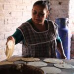 A woman prepares tortillas in a rustic setting in Usmajac, showcasing traditional Mexican cooking methods.