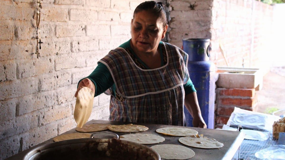 A woman prepares tortillas in a rustic setting in Usmajac, showcasing traditional Mexican cooking methods.