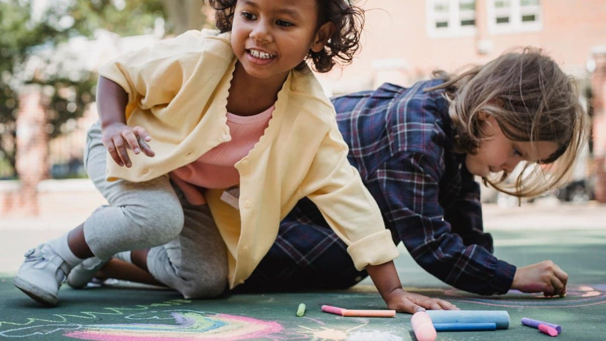Children enjoying outdoor artwork with colored chalk on a sunny day.