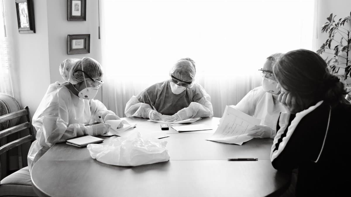 Group of healthcare workers in PPE having a discussion at a table indoors.